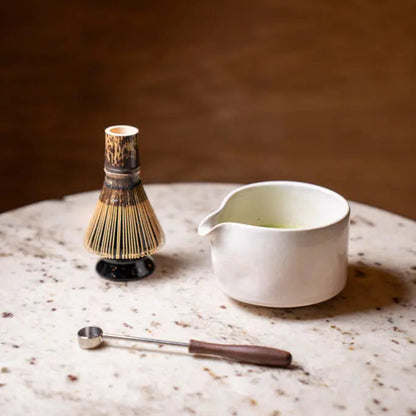 Tea-making tools including a whisk, chasaku, and chawan on a marble surface with a dark background.