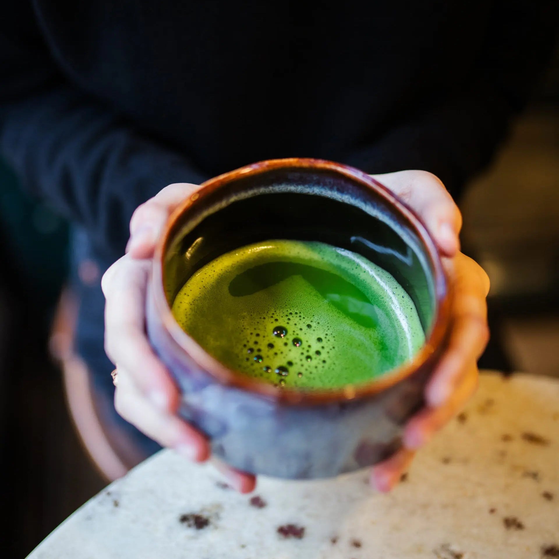 Person holding a ceramic mug with green tea