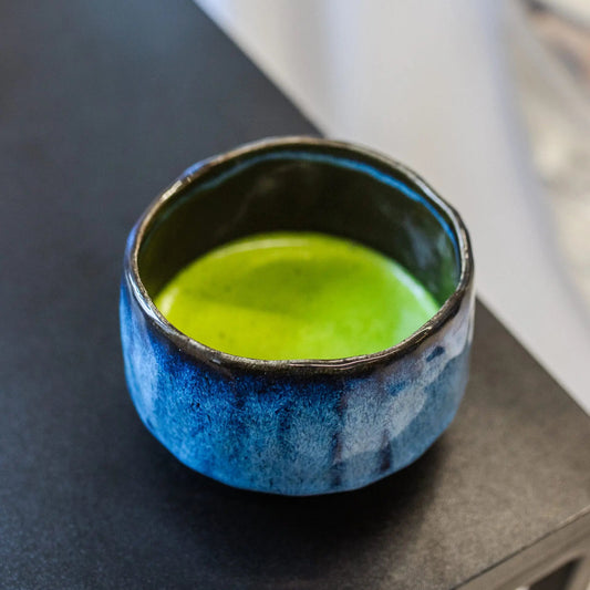 Blue ceramic bowl with green liquid on a dark surface