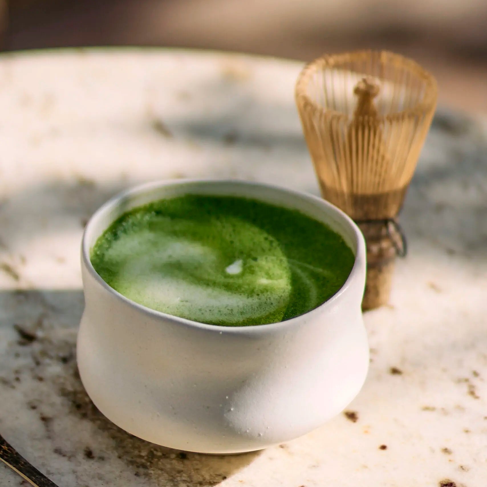 Cup of green tea with a wooden whisk on a stone surface