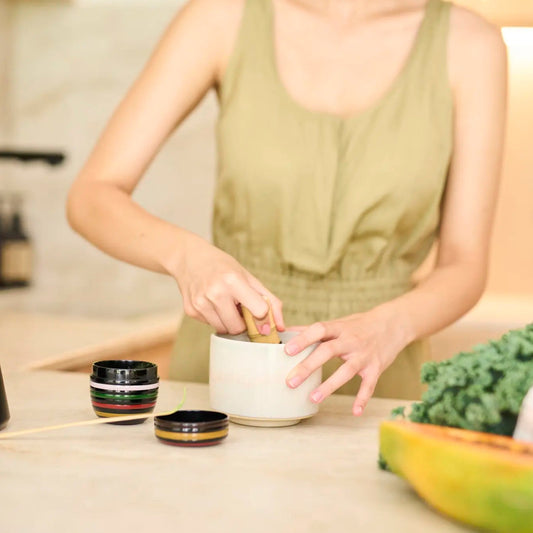Woman preparing a drink in a kitchen with various items on the counter.
