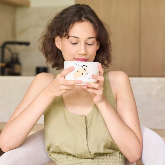 Woman sitting on a couch holding a mug with a cozy indoor setting.