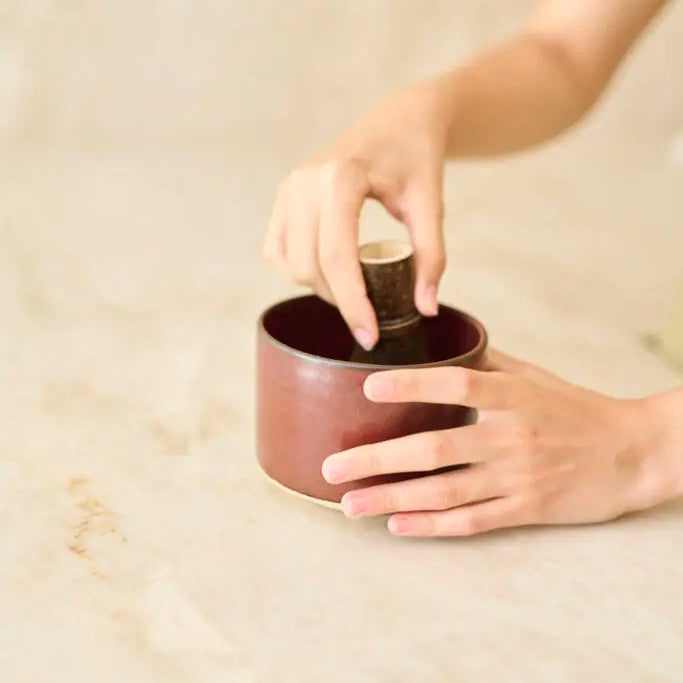 Person holding a small brown ceramic cup with a wooden handle on a beige background