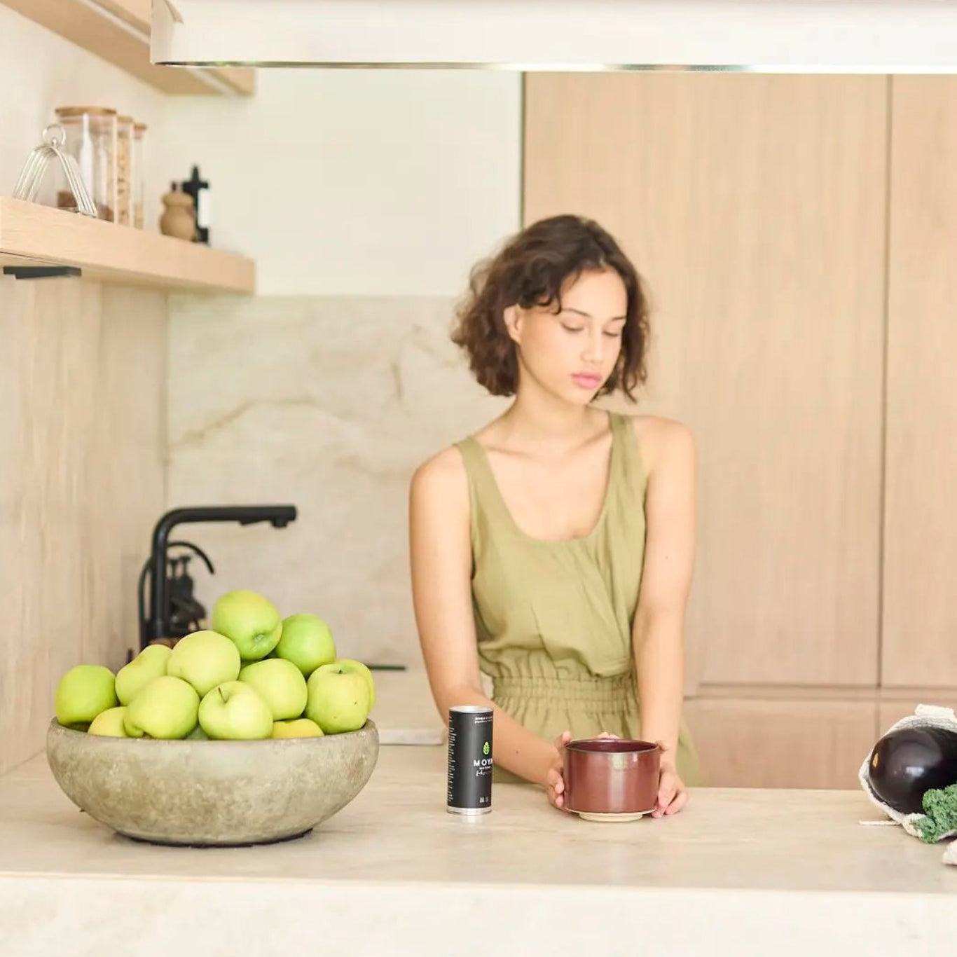 Woman standing in a modern kitchen with a bowl of apples on the counter.