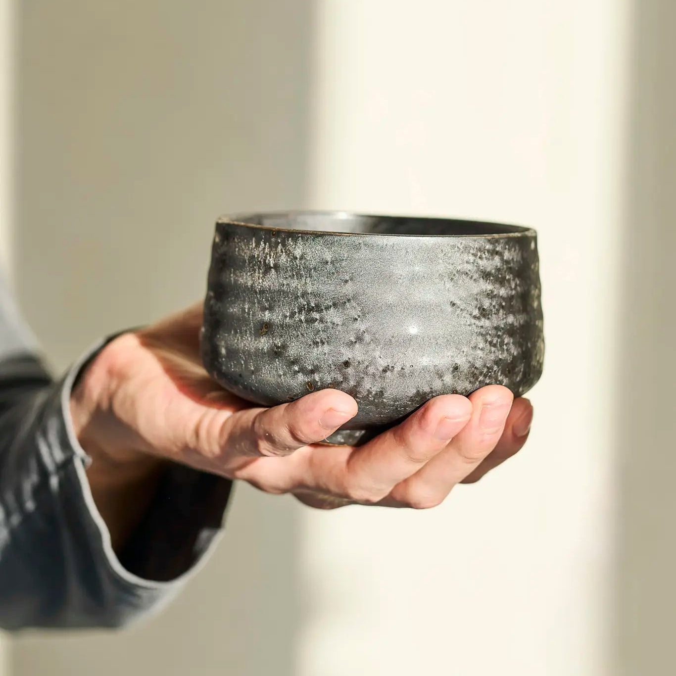 Person holding a textured ceramic bowl against a neutral background