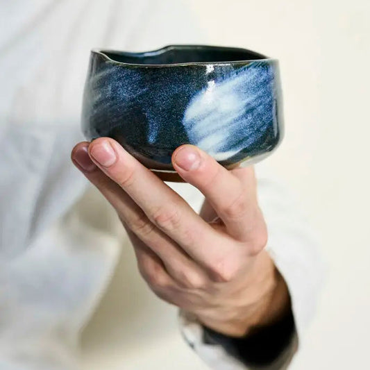 Person holding a ceramic bowl with a blue speckled design against a neutral background