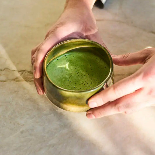 Person holding a green ceramic cup filled with a green liquid on a textured surface