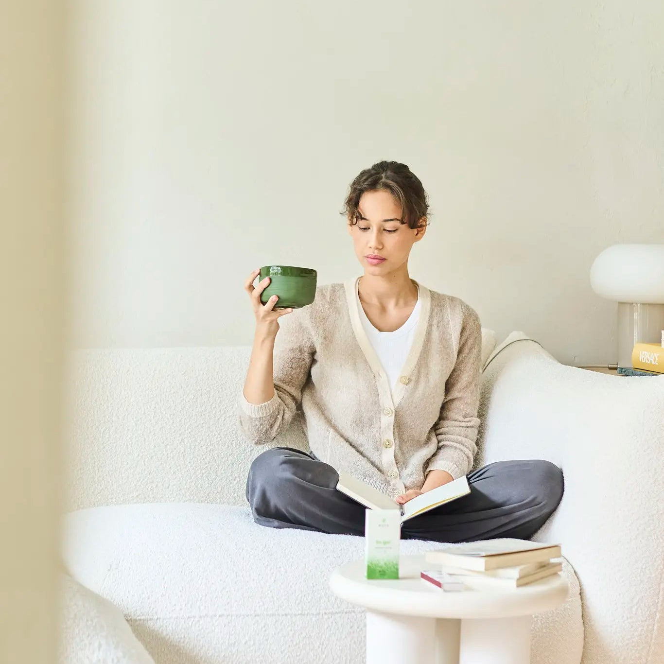 Woman sitting on a couch holding a green mug in a minimalistic living room.