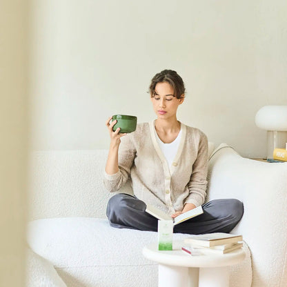 Woman sitting on a couch holding a green mug in a minimalistic living room.